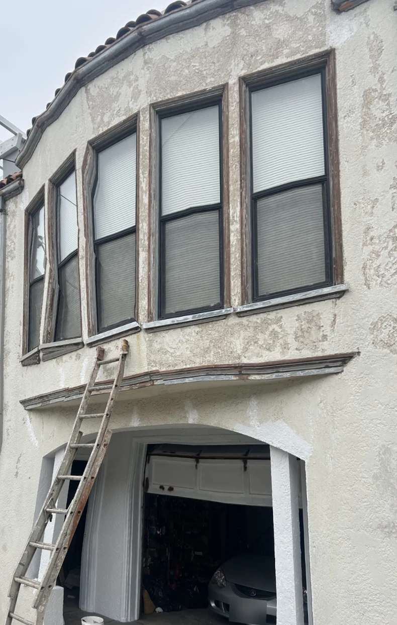 House front before painting, with peeling beige stucco, brown trim and a ladder